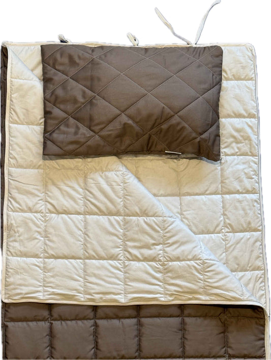 Die Kissenhülle „Essential“ besteht aus einer gesteppten, beige-braunen Unterlage und einem dazu passenden braunen, wärmeisolierenden orthopädischen Reisekissen. Beide sind mit Rauten- und Quadratmustern gesteppt; die Unterlage verfügt über Befestigungsschlaufen an den Ecken und ist teilweise gefaltet, sodass beide Seiten sichtbar sind.