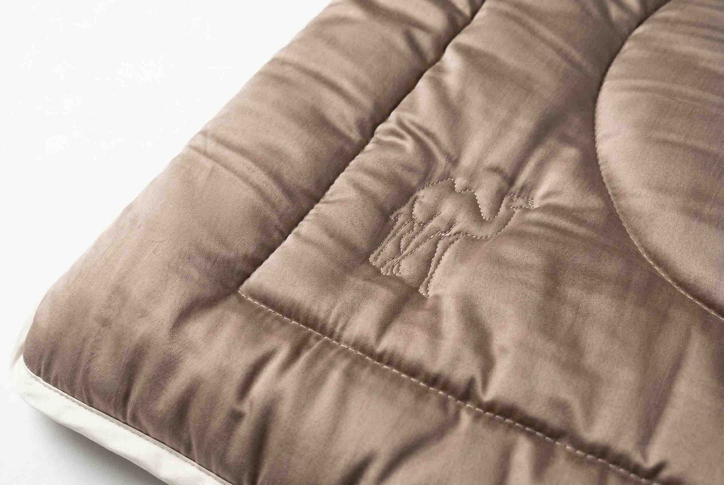 Nahaufnahme des Origobag Essential Kamelhaar: eine braune, gesteppte Bettdecke aus nachhaltigen Materialien mit aufgesticktem Kamel-Umriss und rechteckigem Muster – perfekt für gemütliche Nächte oder als zusätzliche Schicht beim Camping.