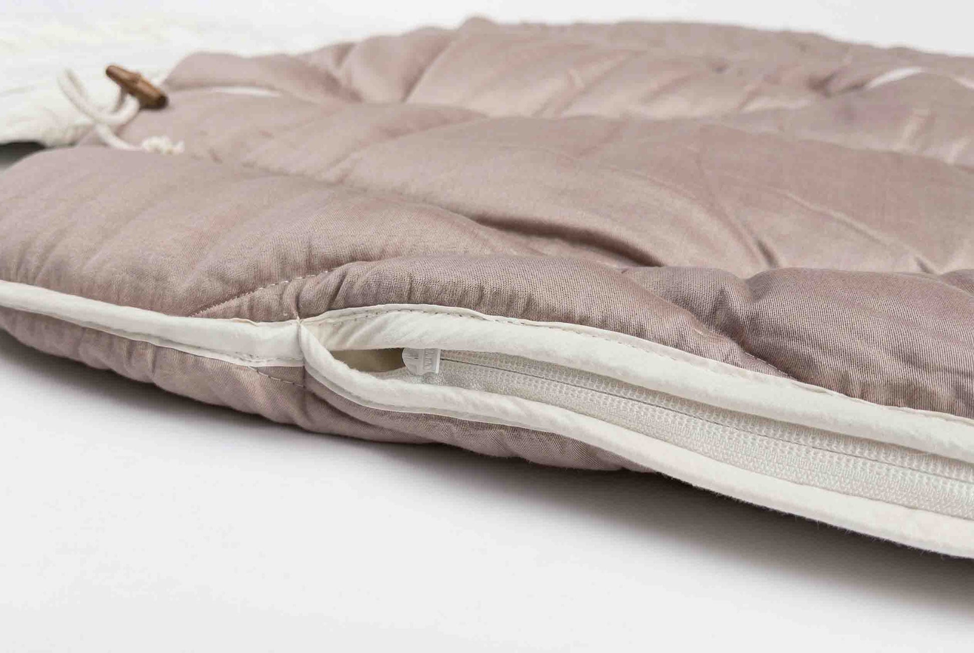Nahaufnahme des Origobag Premium Baumwolle Seide in Hellrosa mit einem teilweise geöffneten weißen Reißverschluss, die die weiche Stoffstruktur und die Nähdetails für maximalen Schlafkomfort hervorhebt.