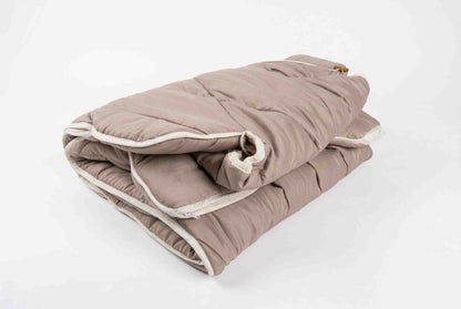Eine dicke, hellbraune Origobag Premium Kamelhaar-Steppdecke ist ordentlich auf einem schlichten weißen Hintergrund gefaltet; sie verfügt über weich gepolsterten Stoff und eine weiße Einfassung für optimalen Schlafkomfort.